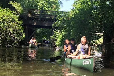 Three paddlers in a canoe passing under an old wooden bridge in Köpenick, Berlin