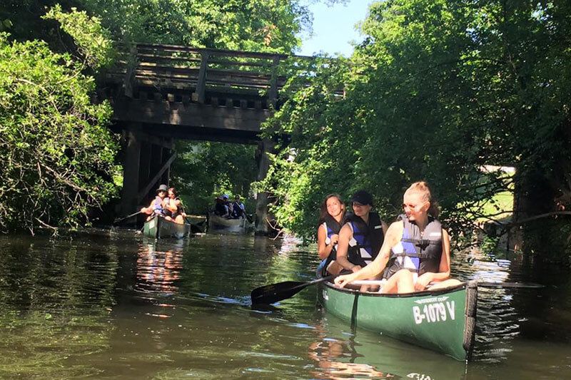 Three paddlers in a canoe passing under an old wooden bridge in Köpenick, Berlin