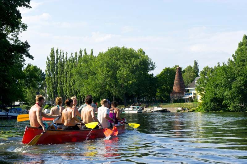 Paddlers in a red canoe on the water in Köpenick, Berlin, with a historic brick tower behind
