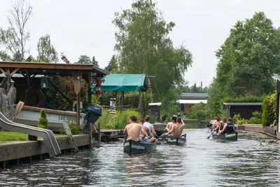 Canoes paddling along a narrow canal lined with boathouses and gardens in Neu Venedig, Berlin
