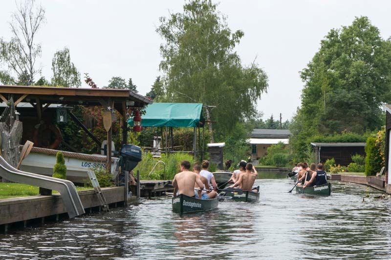Canoes paddling along a narrow canal lined with boathouses and gardens in Neu Venedig, Berlin