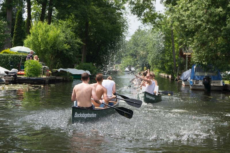 Paddlers splashing water between canoes on a leafy canal in Neu Venedig, Berlin