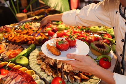 Chef holding a plate of stuffed tomatoes over a colourful buffet