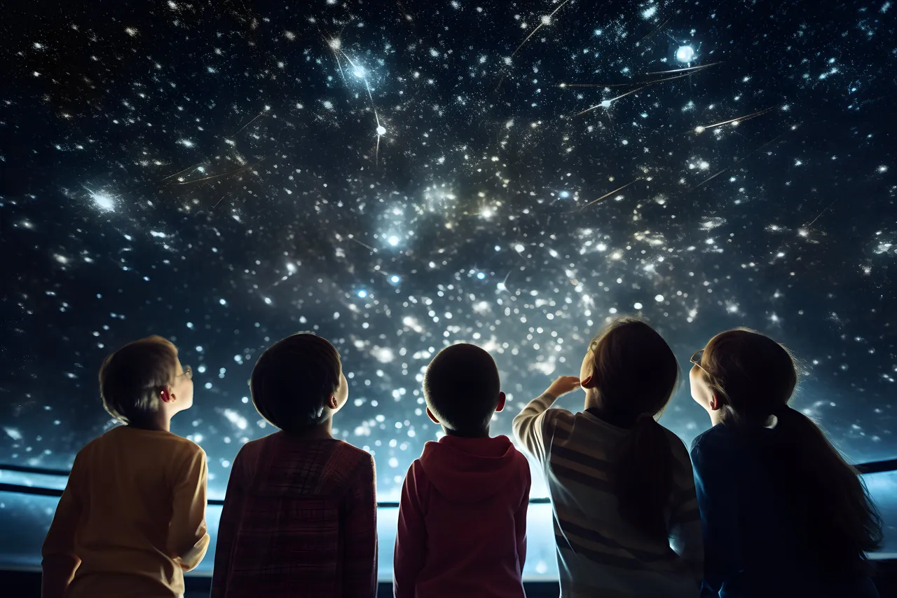 Rear view of a group of young children looking up in awe at a bright constellation and star projection inside a planetarium.