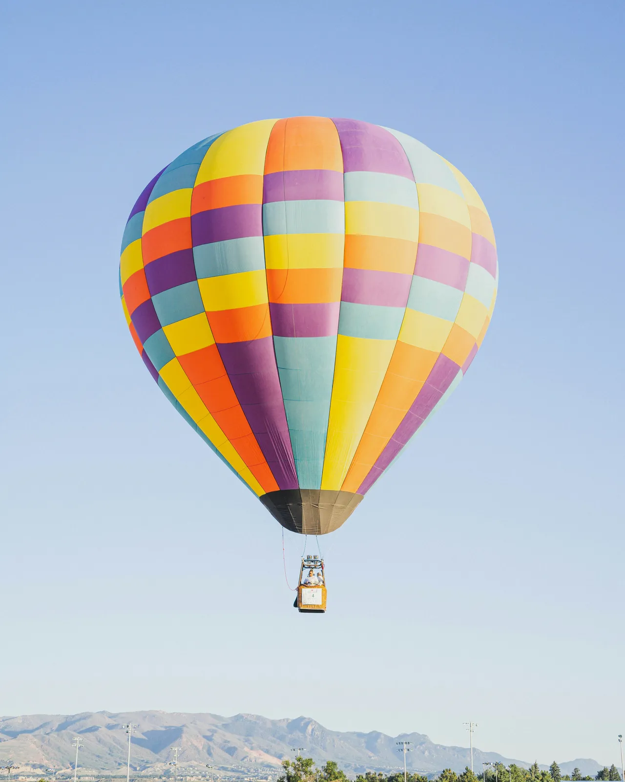 Several vibrant, multi-colored hot air balloons floating together in a clear blue sky.