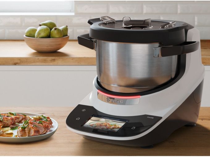 Stainless steel kitchen machine with digital display on a countertop next to a plate of grilled chicken