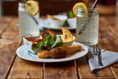Plate with falafel, spring roll and salad next to lemonade on a rustic wooden table