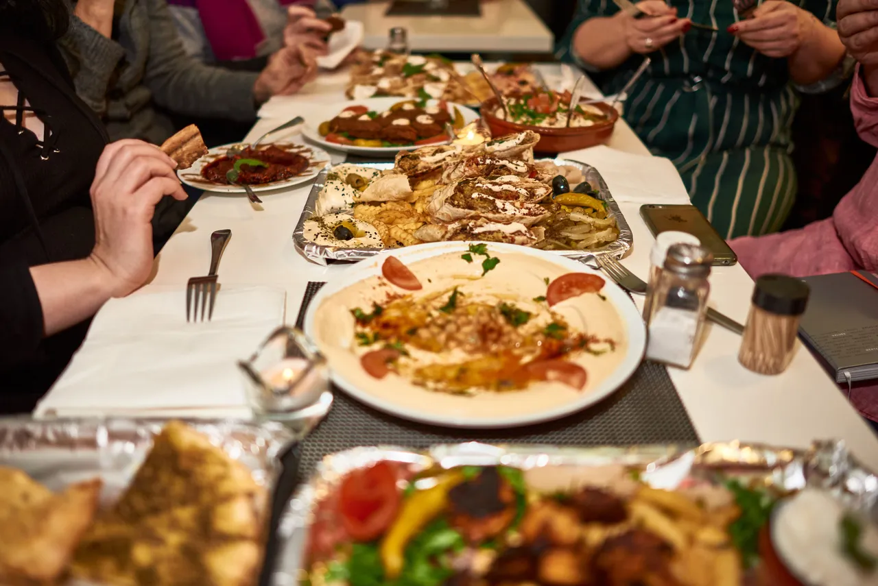 Group of guests sharing hummus, grilled meat and mezze at a long table