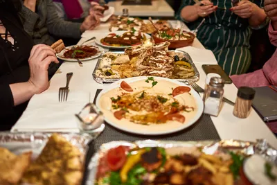 Group of guests sharing hummus, grilled meat and mezze at a long table