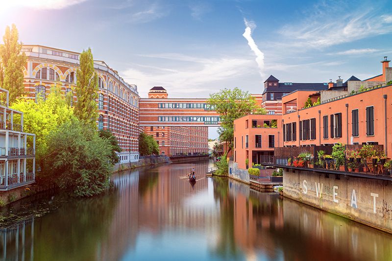 Canal lined with restored red-brick industrial buildings in Leipzig under a blue sky