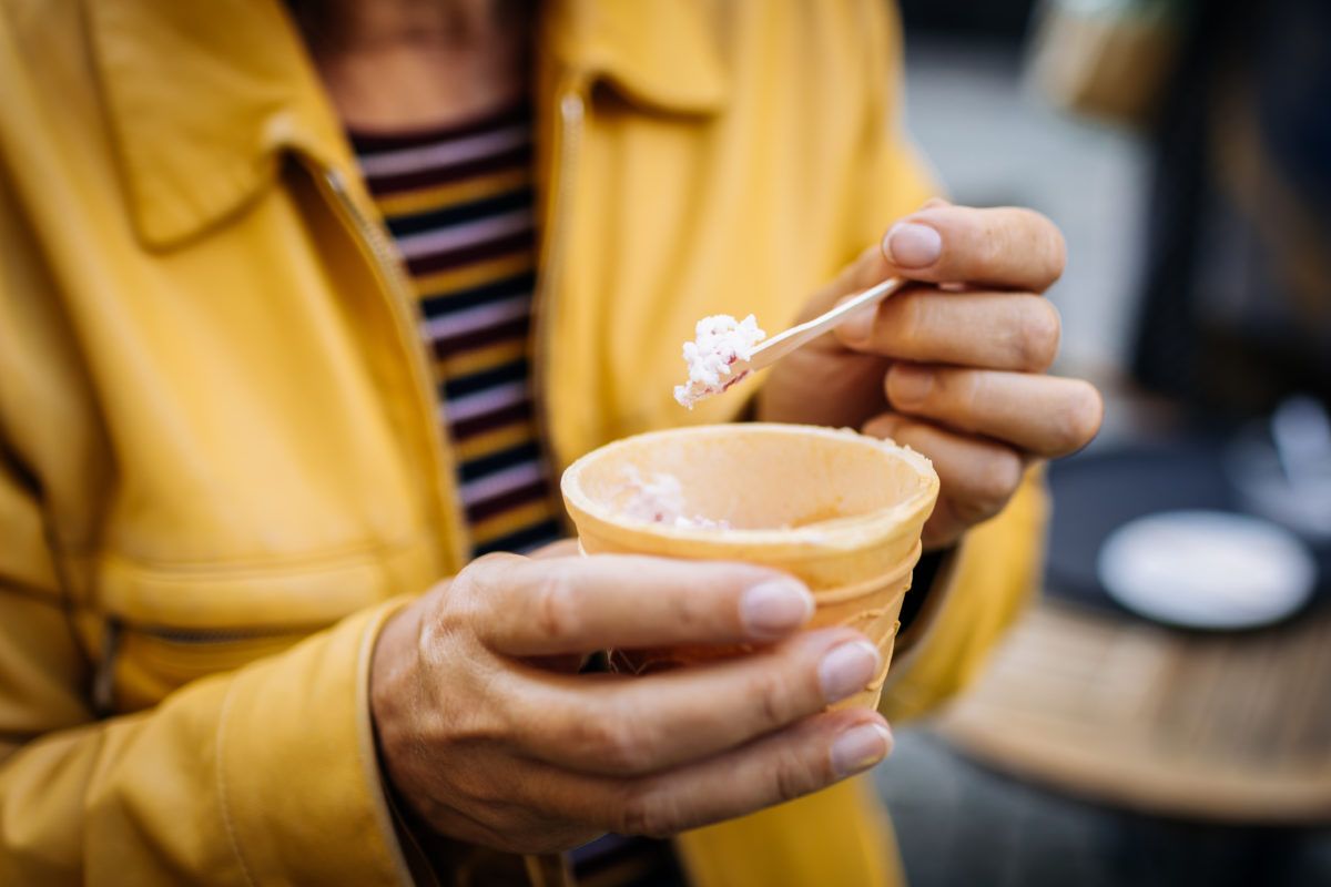 Woman in a yellow jacket tasting ice cream from a cone