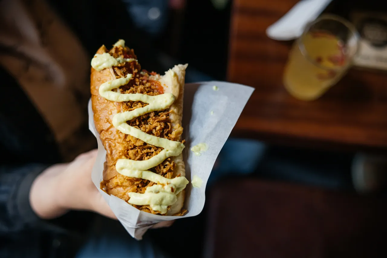 Hand holding a loaded hot dog topped with sauce and crispy onions