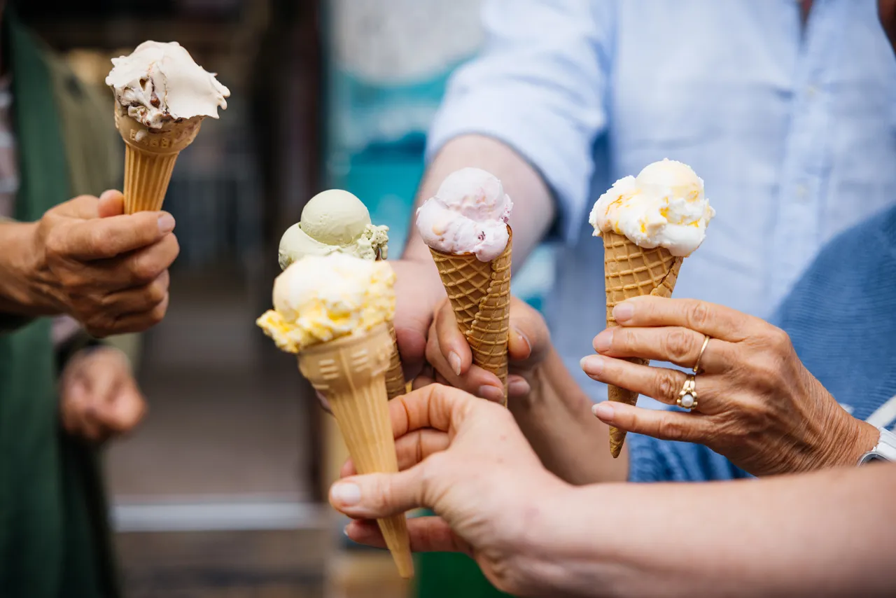 Several hands holding ice cream cones with different flavours