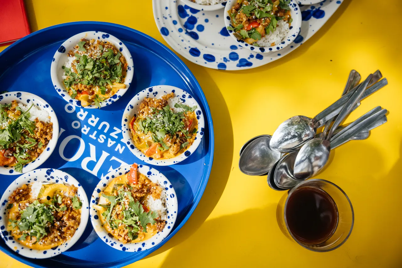 Overhead view of colourful mezze bowls on a blue tray on a yellow table