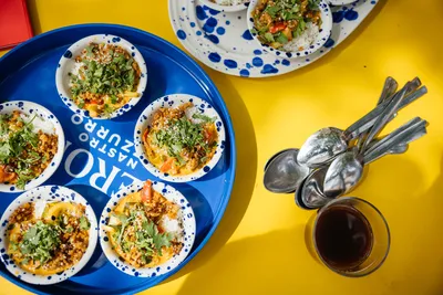 Overhead view of colourful mezze bowls on a blue tray on a yellow table