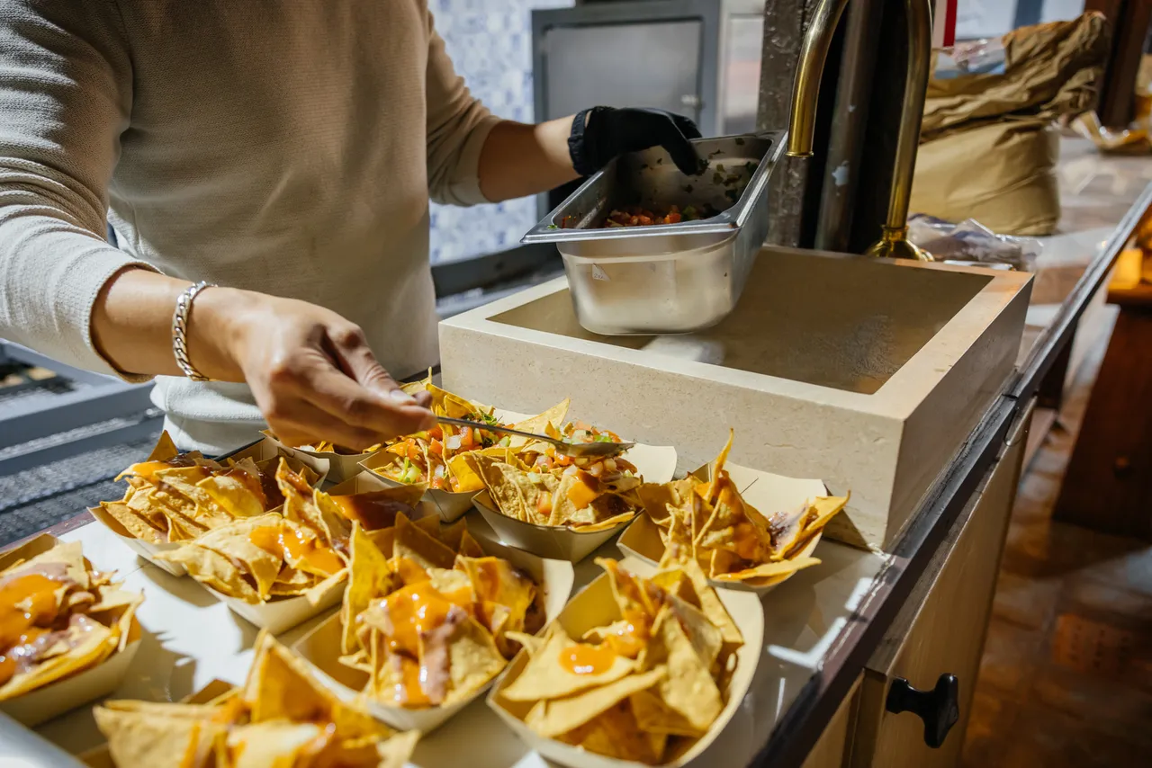 Nachos with cheese sauce being served into paper boats at a food stop