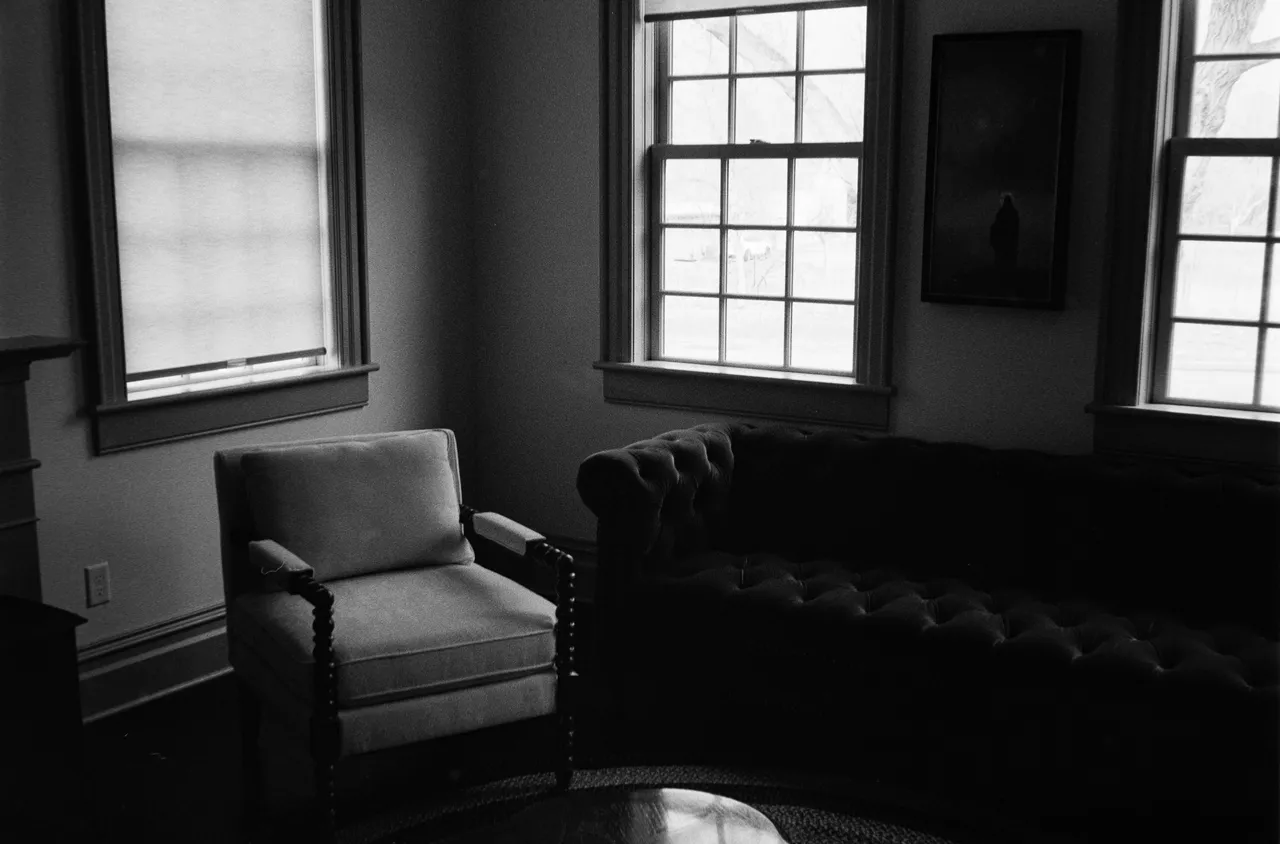 Dimly lit room with a leather chesterfield sofa and an armchair, in black and white
