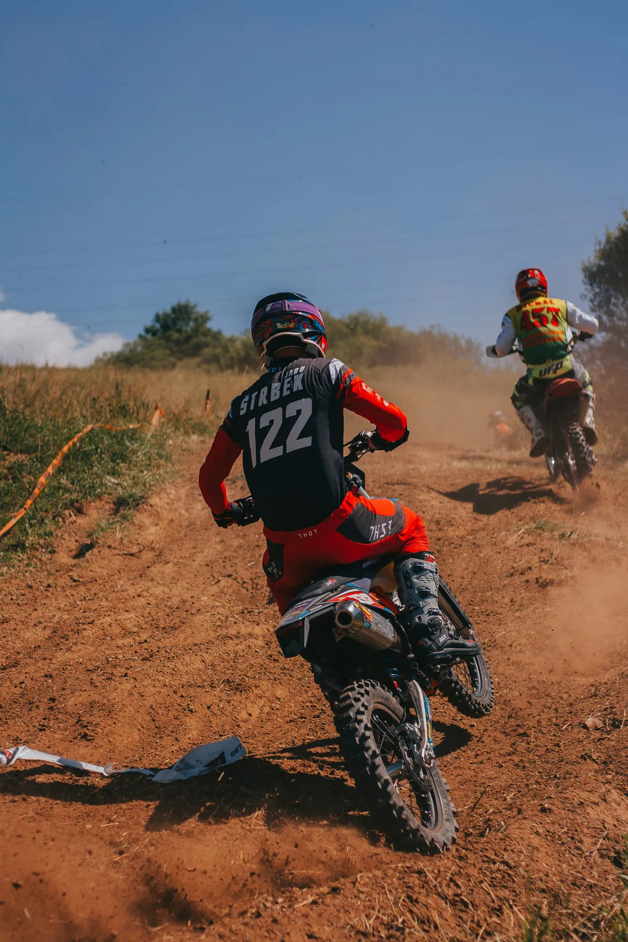 A motorcyclist stands up on the footpegs of a dirt bike while riding along a dirt path.