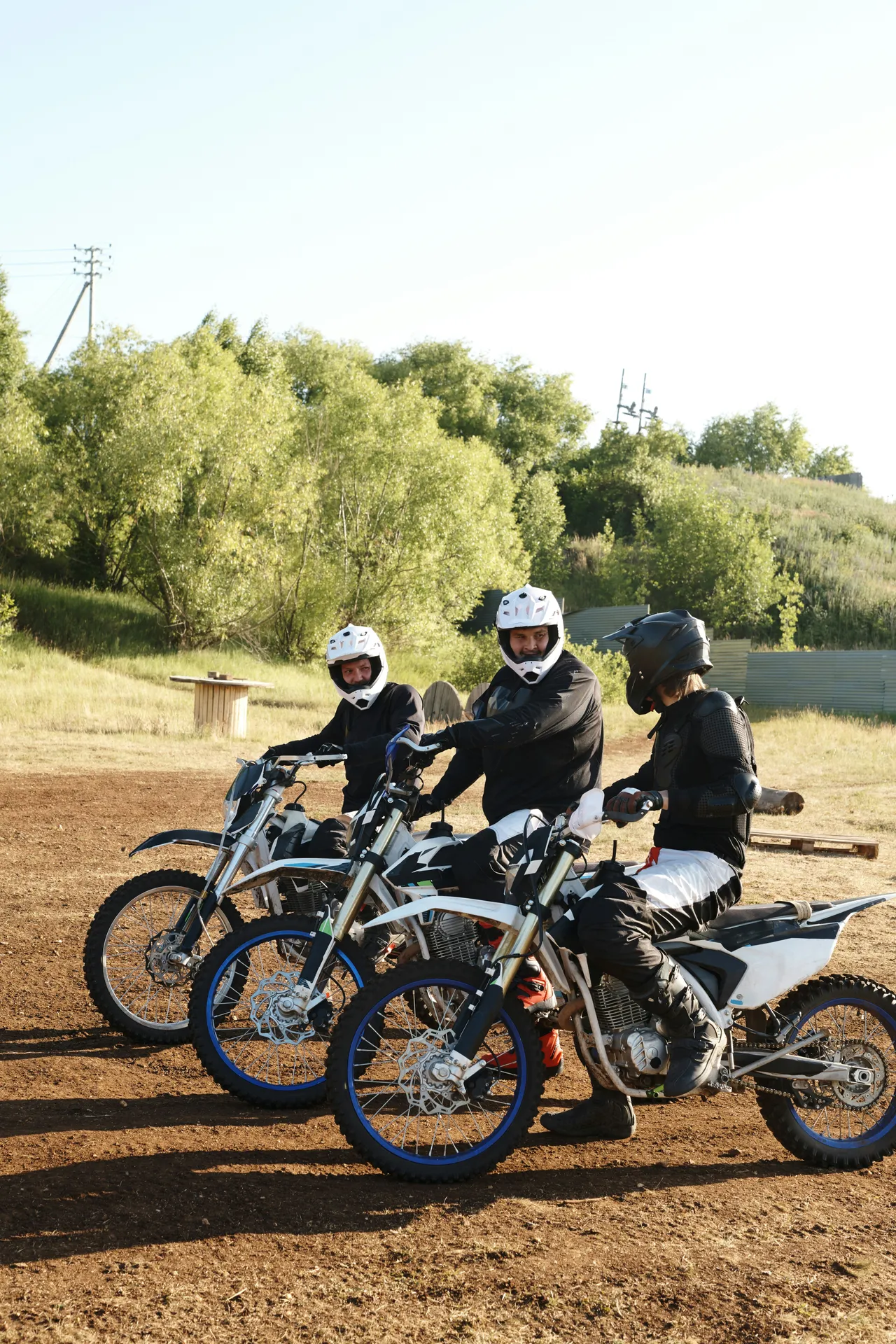 Three enduro riders in full protective gear and helmets prepare to navigate a track. 