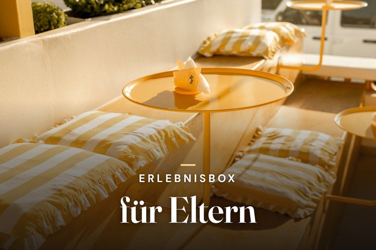 Experience gift box for parents – sunlit terrace bench with yellow striped cushions and a round yellow side table