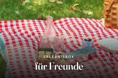 Experience gift box for friends – picnic on a red-and-white checked blanket with a glass bottle, jars and a wicker basket