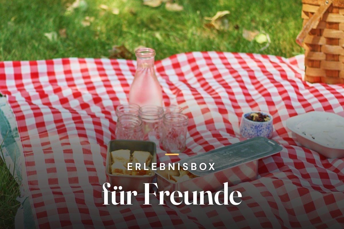 Experience gift box for friends – picnic on a red-and-white checked blanket with a glass bottle, jars and a wicker basket