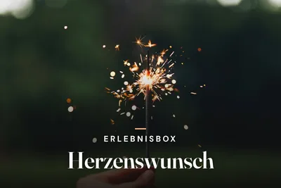 Hand holding a sparkler against a dark green background, with the text "Erlebnisbox Herzenswunsch"
