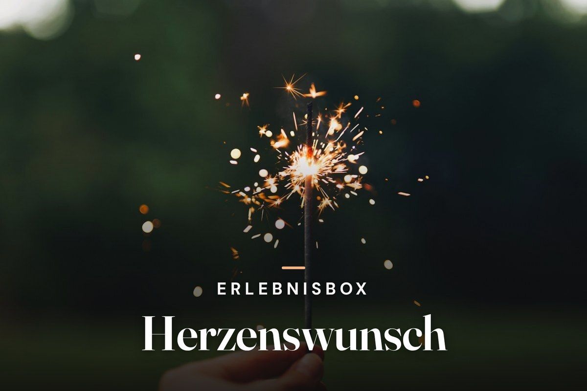 Hand holding a sparkler against a dark green background, with the text "Erlebnisbox Herzenswunsch"