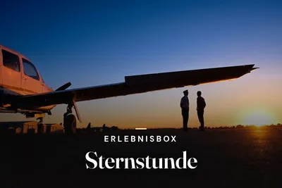 Pilot and passenger standing under the wing of a small aircraft at sunset, with the text "Erlebnisbox Sternstunde"