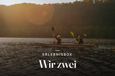 Two people paddling a kayak on a lake at sunset, with the text "Erlebnisbox Wir zwei"