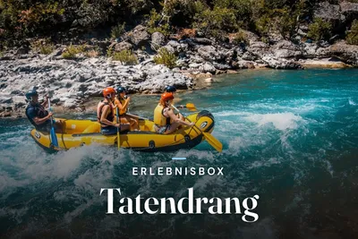 Group in helmets and life jackets white water rafting on a turquoise river, with the text "Erlebnisbox Tatendrang"