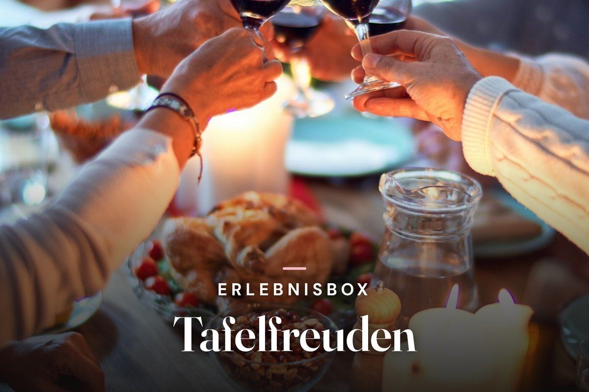 Friends raising glasses of red wine over a candlelit dinner table, with the text "Erlebnisbox Tafelfreuden"