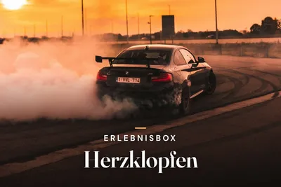 Black sports car drifting on a track with tire smoke at sunset, with the text "Erlebnisbox Herzklopfen"