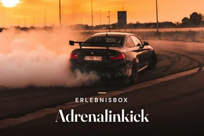 Black sports car drifting on a track at sunset, surrounded by a cloud of tyre smoke, with the title "Erlebnisbox Adrenalinkick".