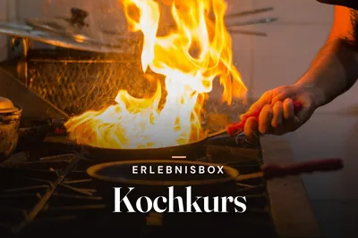 Chef flambéing food in a pan over a gas stove with high flames, overlaid with the title Erlebnisbox Kochkurs