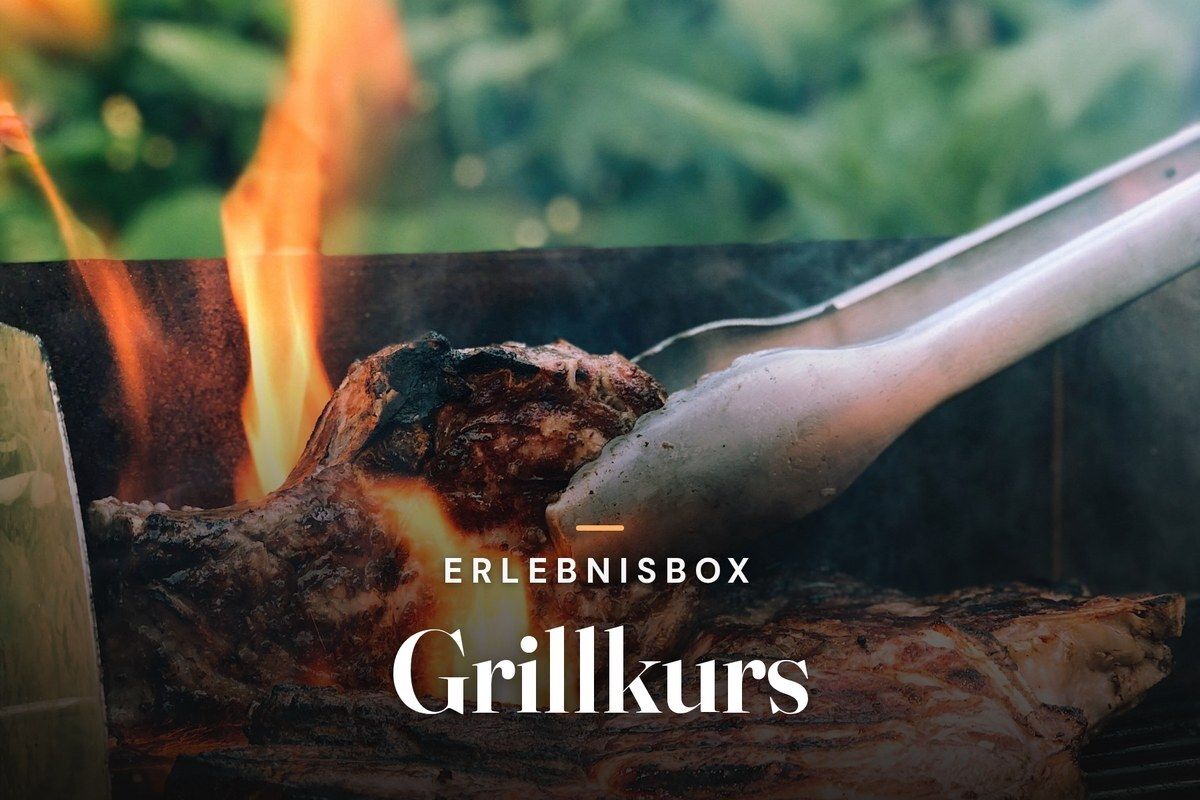 Tongs turning a thick steak over open flames on a grill, with green foliage in the background, with the text “Erlebnisbox – Grillkurs”
