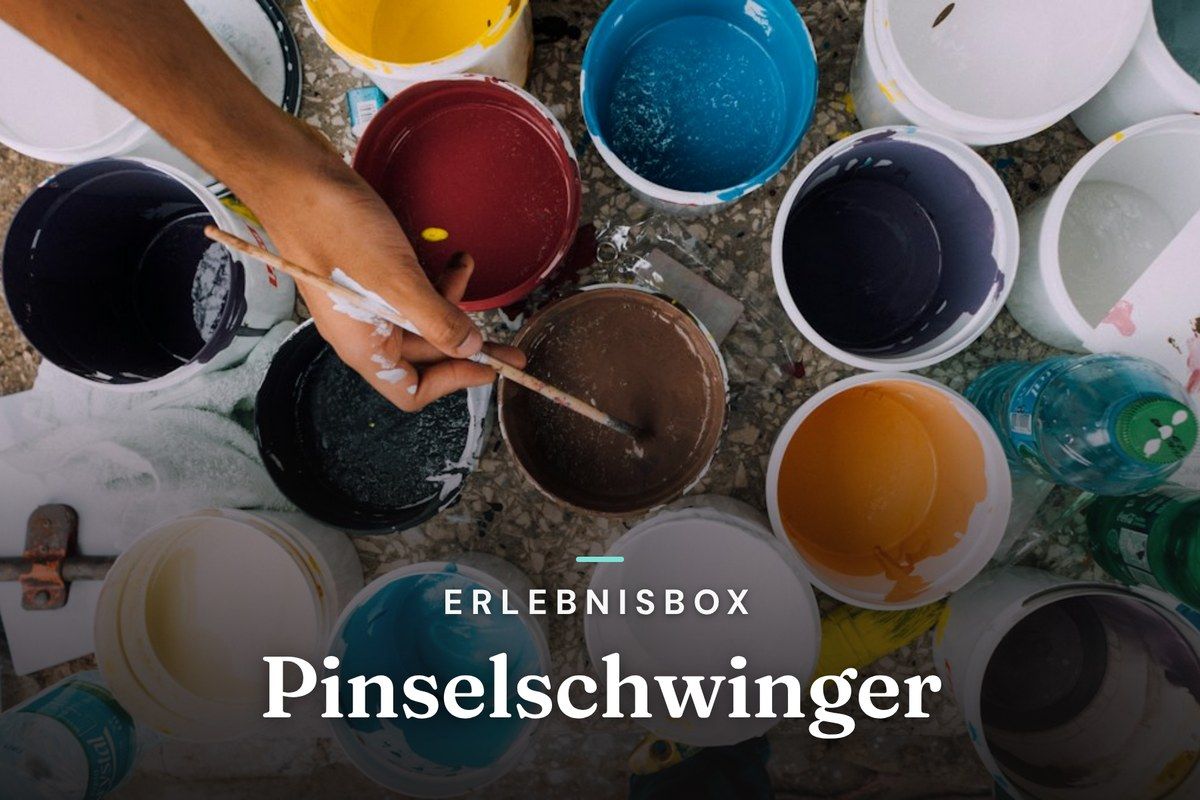 Hand dipping a brush into colorful open paint buckets