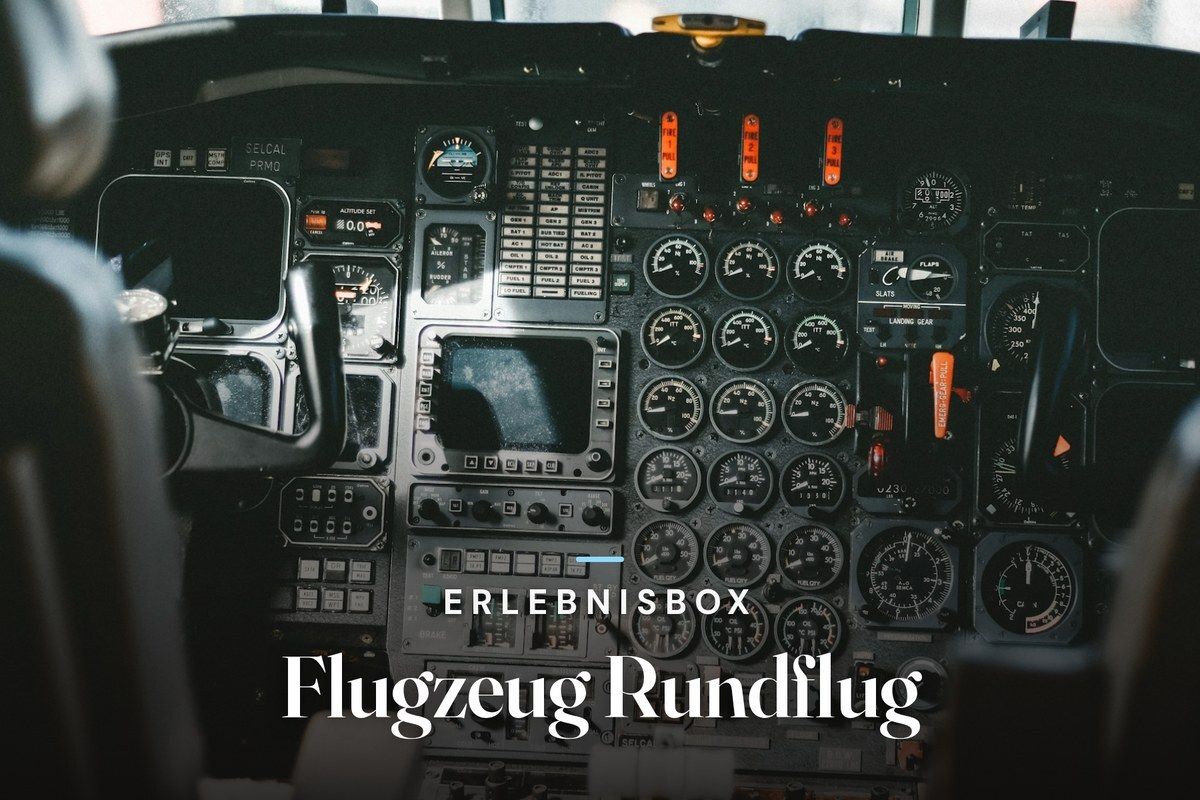 Cockpit of a small aircraft with an instrument panel full of round gauges, switches and red fire handles, with the text “Erlebnisbox – Flugzeug Rundflug”