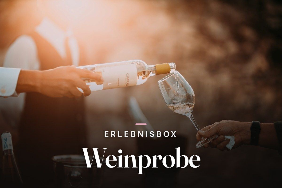 Hand pouring white wine from a bottle into a glass held by a guest, in warm evening sunlight, with the text “Erlebnisbox – Weinprobe”