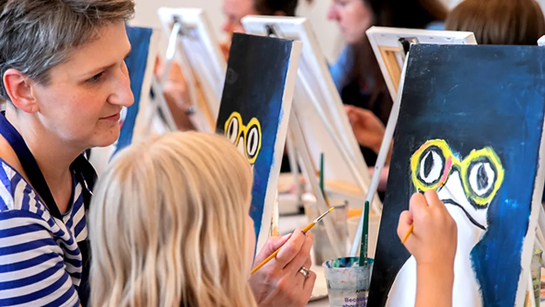 Parent and child painting an animal with yellow glasses on canvas