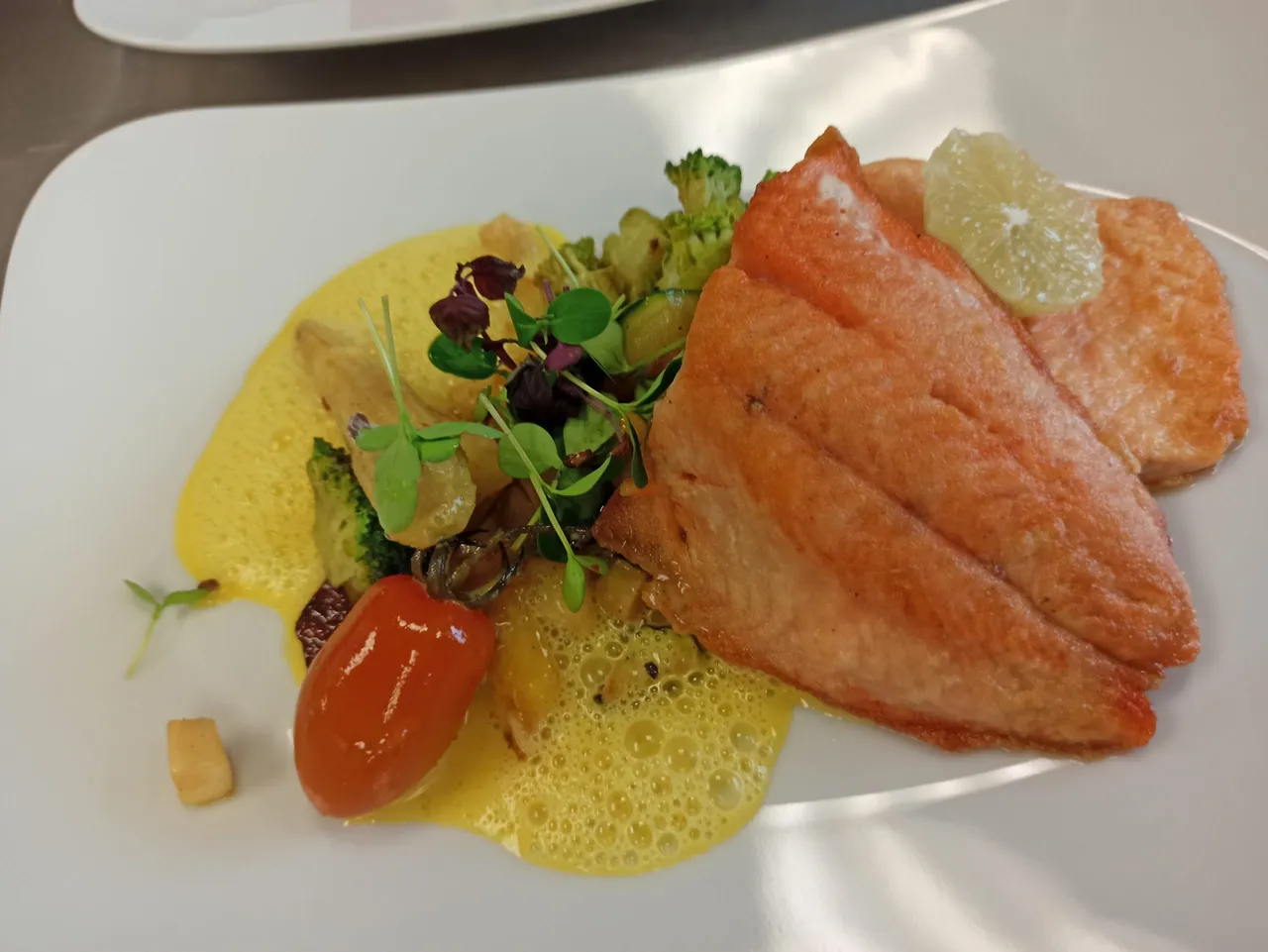 Pan-fried salmon fillet on saffron sauce with vegetables and fresh cress on a white plate