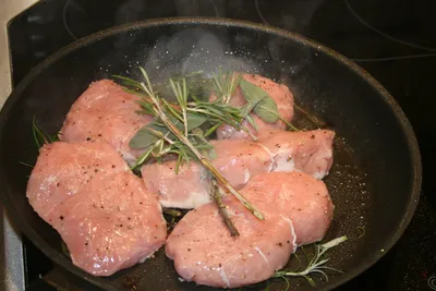 Salmon pieces searing in a frying pan with fresh rosemary sprigs