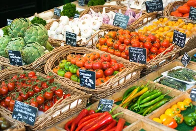 Market stall with fresh vegetables such as tomatoes, peppers, artichokes and garlic in baskets