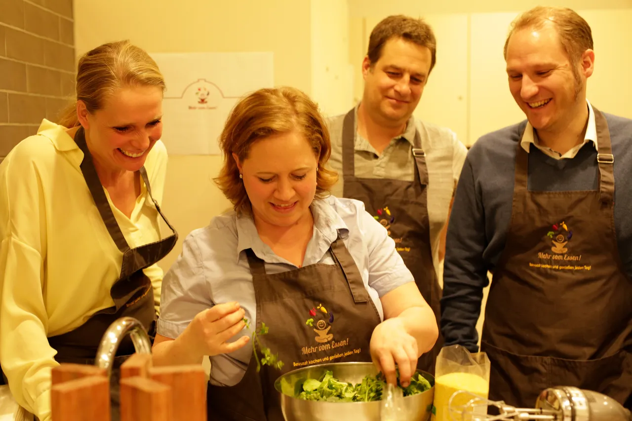 Cooking class group in aprons laughing while preparing a salad together