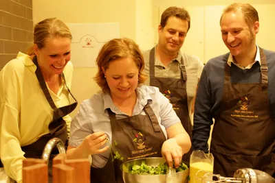 Cooking class group in aprons laughing while preparing a salad together