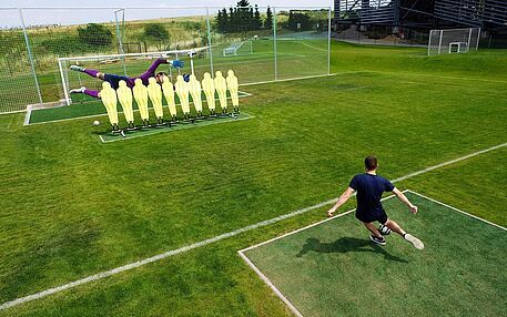 Player taking a shot over a wall of yellow dummies towards a goal on an outdoor footgolf field