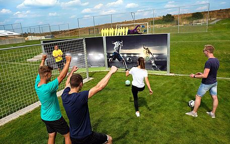 Group of friends cheering while playing footgolf in front of a goal wall