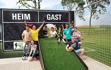 Happy group with footballs posing in front of a home and away scoreboard