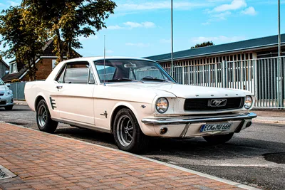 White 1966 Ford Mustang coupé parked on a cobbled street under a blue sky