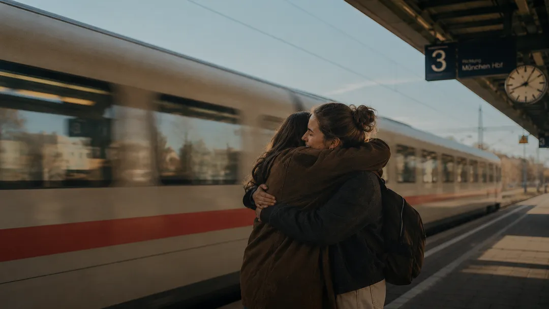 Two friends hugging goodbye on a train platform as a train pulls in